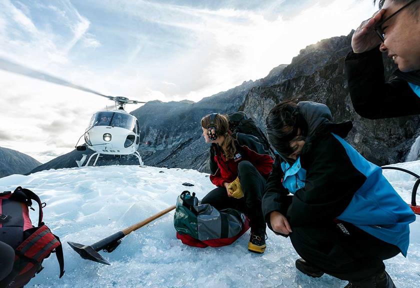 People crouching down on ice looking at helicopter nearby
