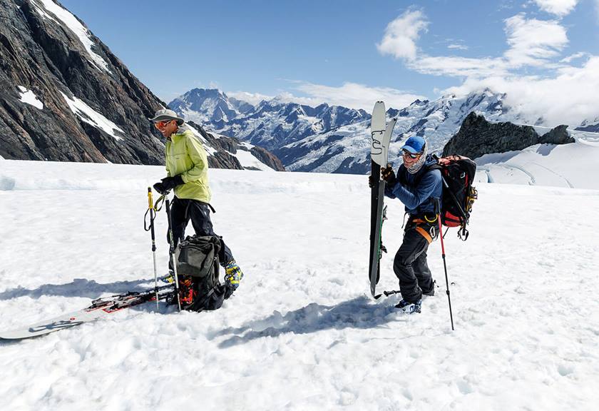 Two people carrying equipment and skis to navigate icy terrain