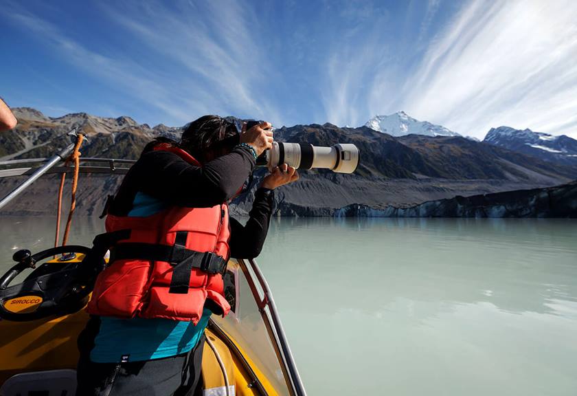 Photographer on boat capturing view on the lake with mountains and clouds in the background