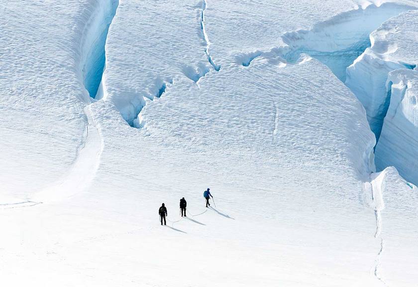 Aerial view of three people behind one another trekking through vast icy plains