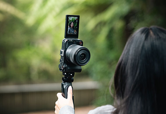 Image of a woman using a Canon camera with its flip screen rotated to the front to take a selfie