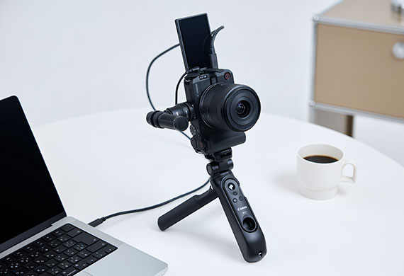 Image of a Canon camera mounted on a mini tripod set on a table amongst a laptop and a cup of coffee