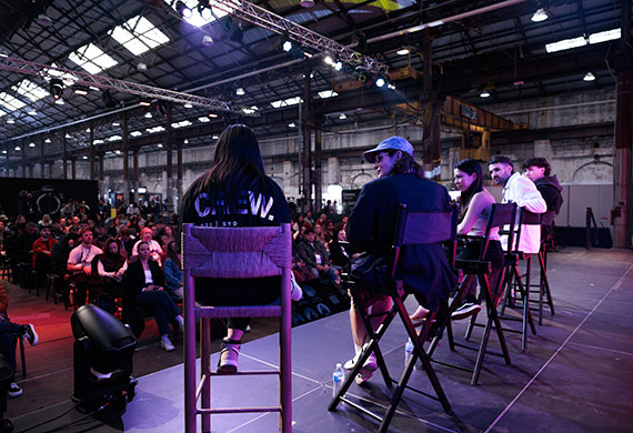 Image of a speaking panel on stage with a packed audience