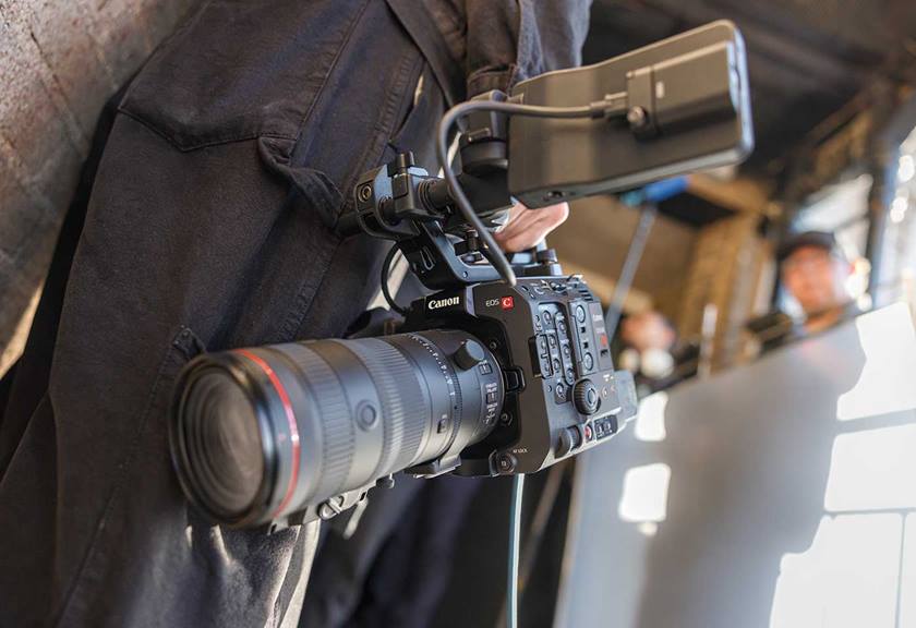 Someone holding cinema camera by their side with long lens attached to it