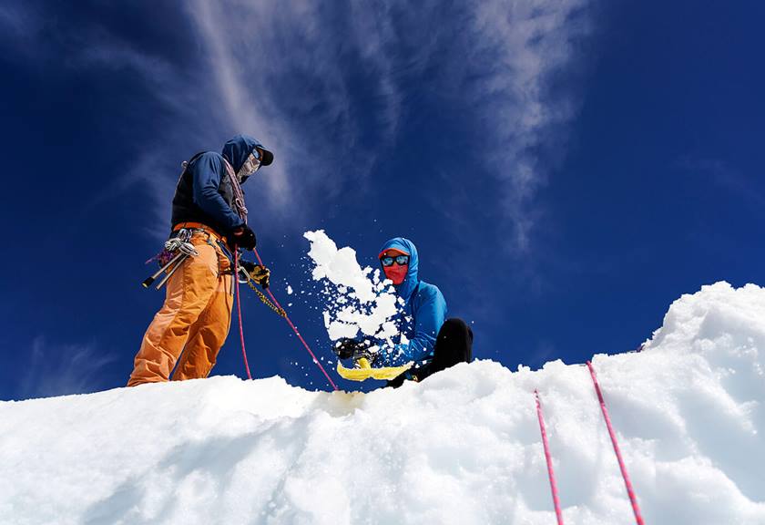 Upwards view of two people in winter equipment throwing snow 