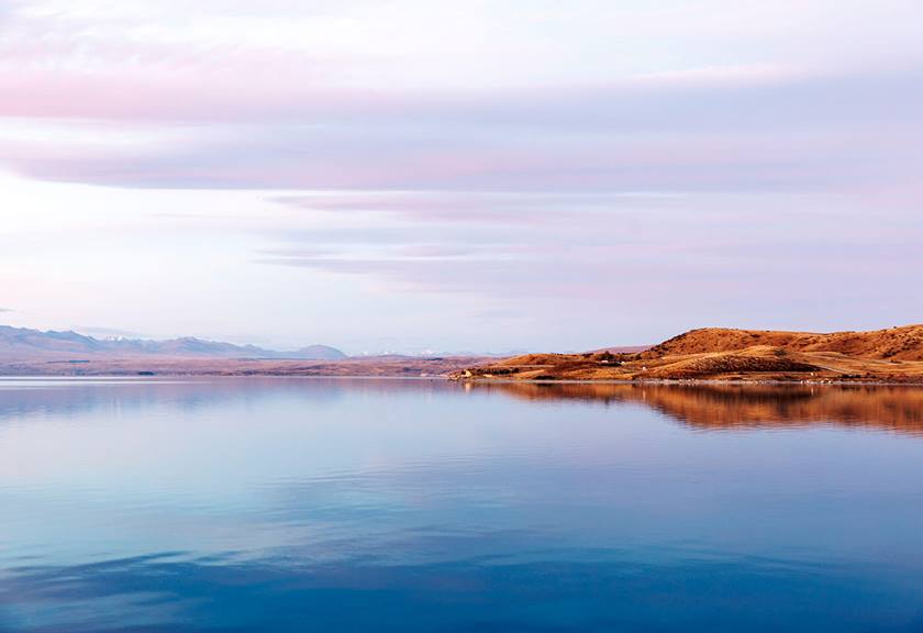 Pastel clouds over grassy hill and still lake