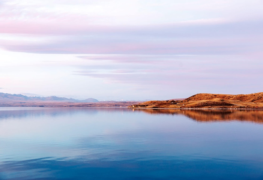Pastel clouds over grassy hill and still lake