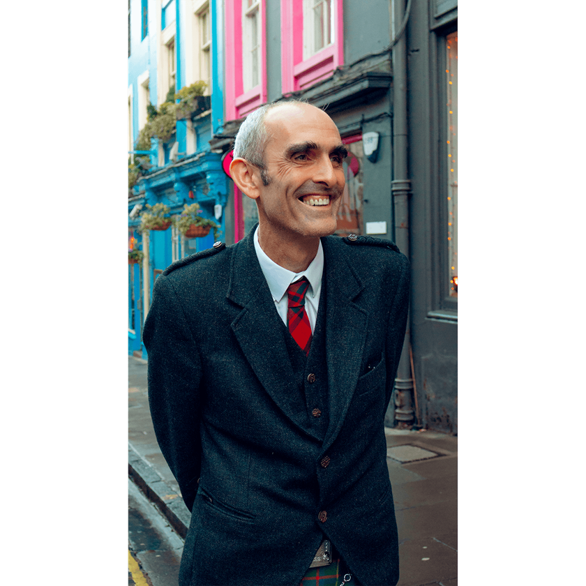 Portrait image of a Scottish gentleman smiling in red tie and black coat
