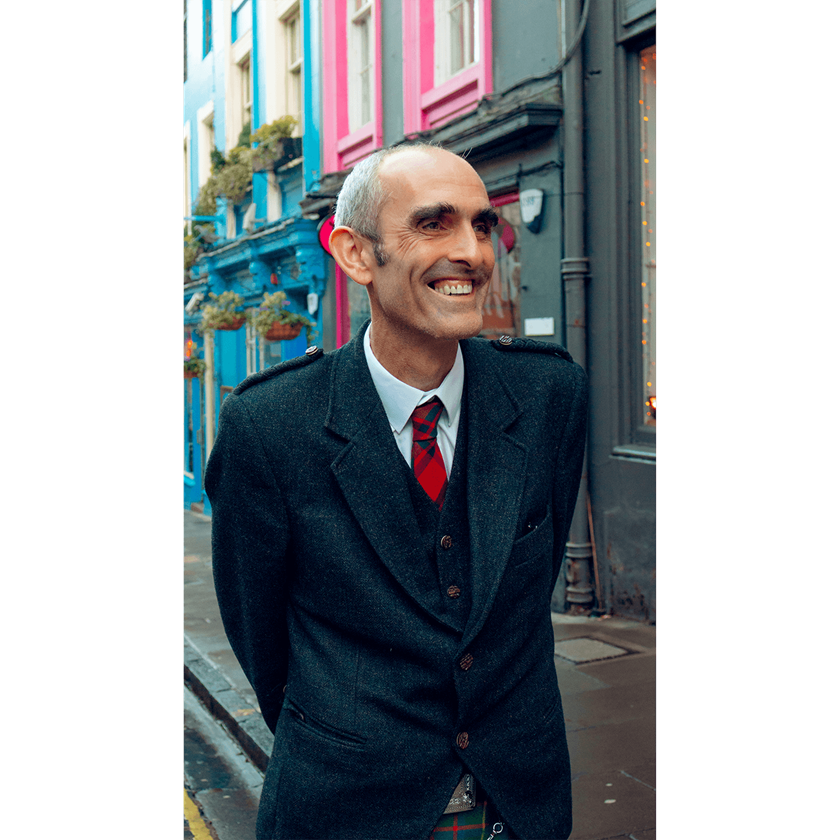 Portrait image of a Scottish gentleman smiling in red tie and black coat