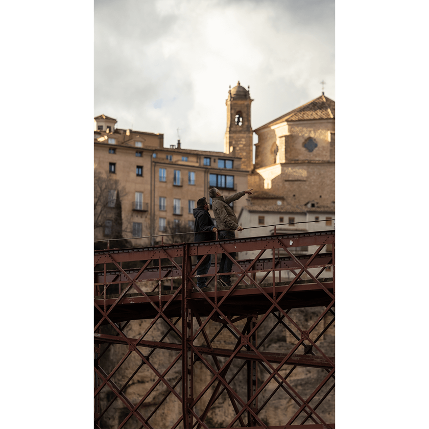 Image of two men standing on red rusty bridge pointing at ornate buildings