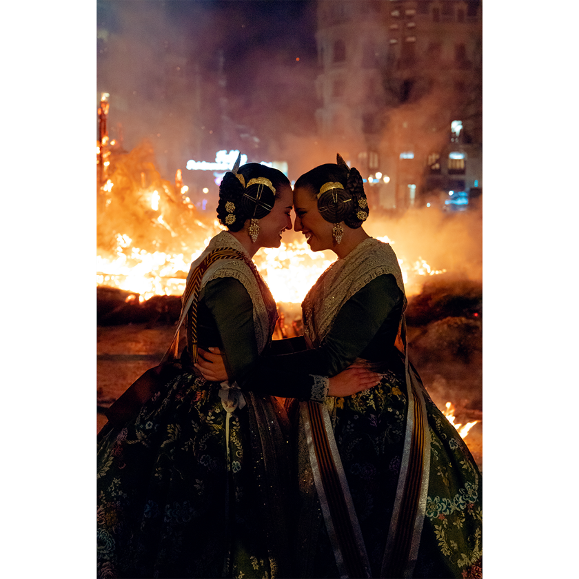 Image of two girls in traditional dress touching foreheads in front of a fire