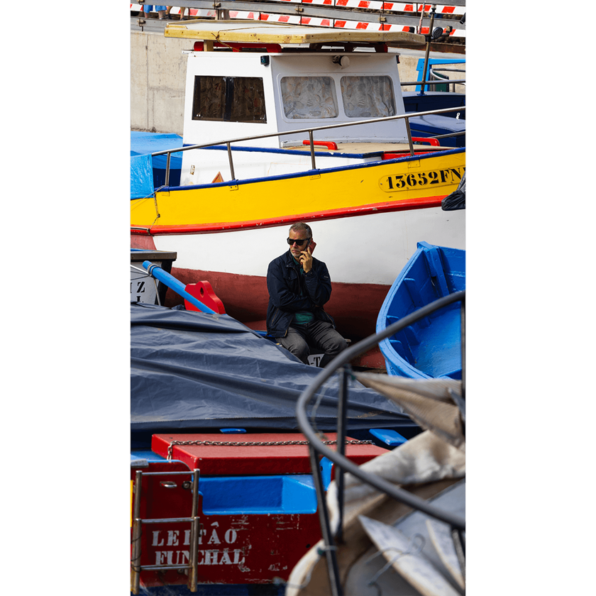 Image of a man in sunglasses and on phone sitting between colourful boats