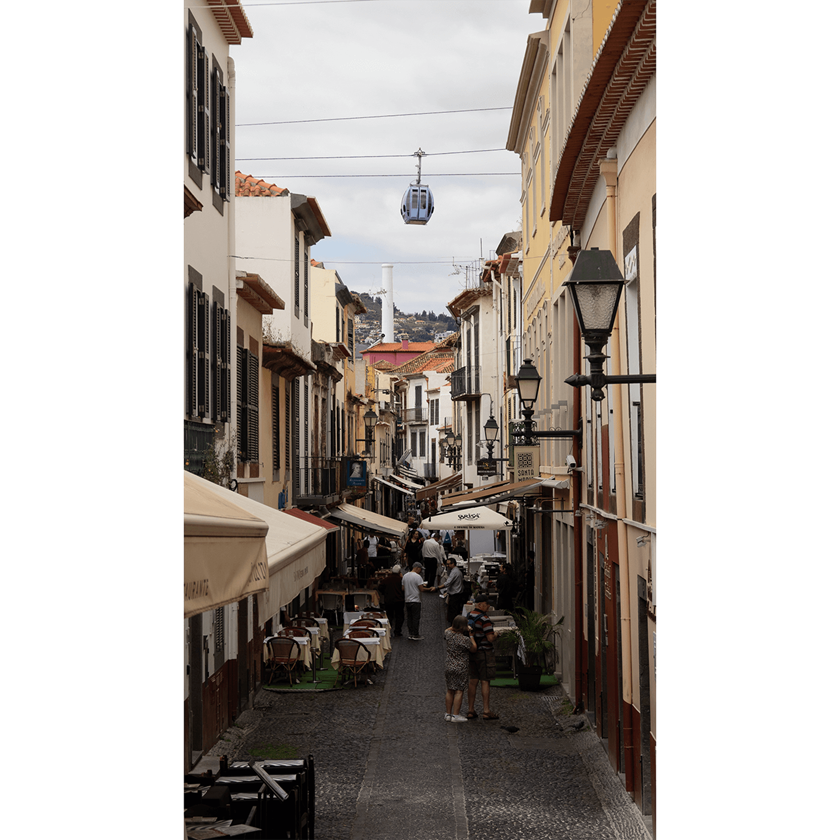 Image of a busy cobblestone street in Madeira, Portugal with cable car hanging in sky