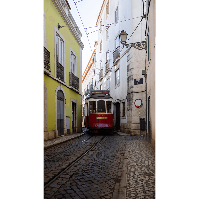 Image of a red tram squeezing through two buildings in old Lisbon street
