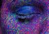 close up of an eye with face covered in multi-coloured paint