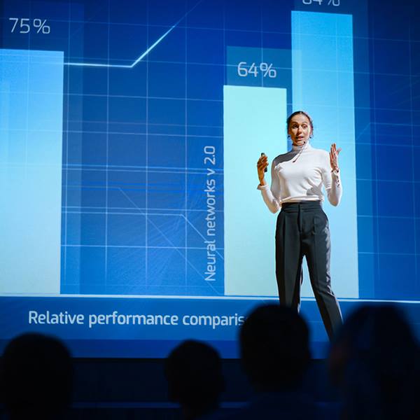 Woman speaking in front of an audience with a chart in the background