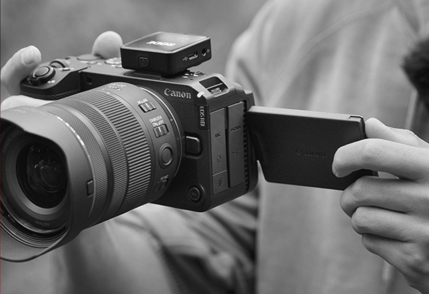 Close-up of a Canon mirrorless camera with a flip-out LCD screen being adjusted by hand.