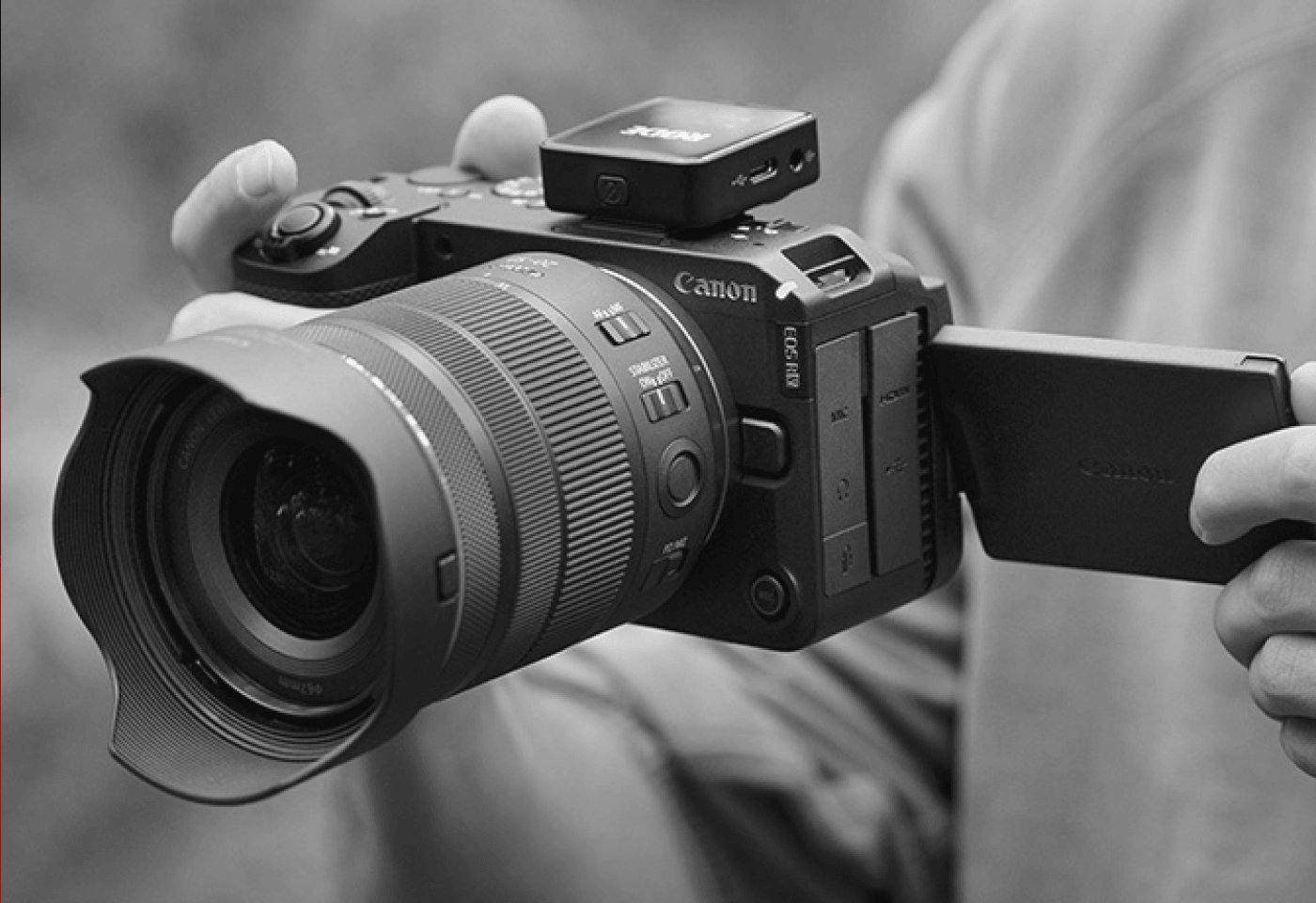 Close-up of a Canon mirrorless camera with a flip-out LCD screen being adjusted by hand.