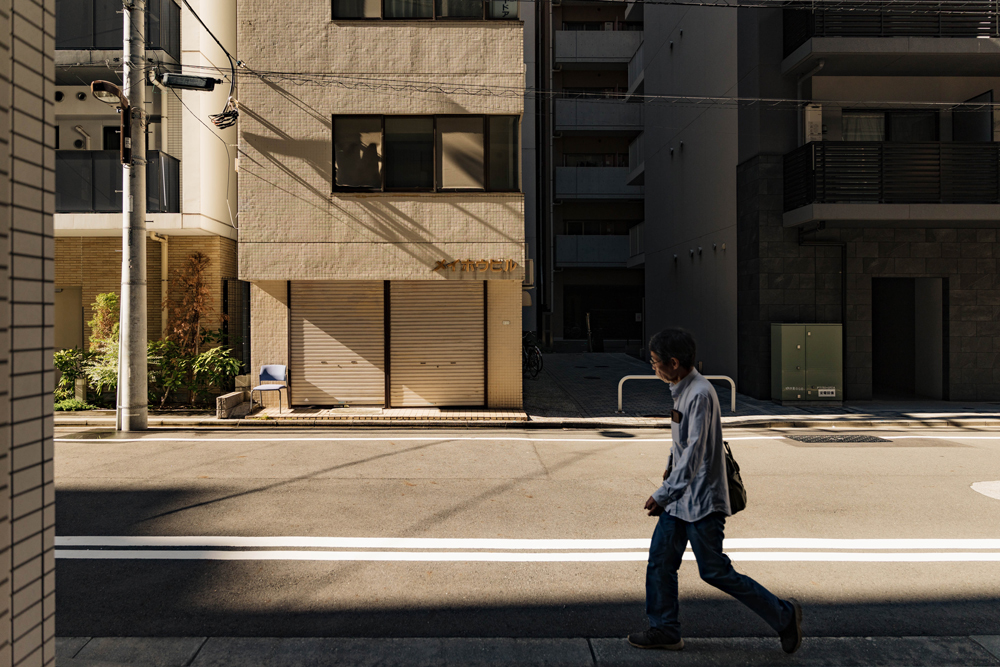 Person walking through a sunlit Tokyo street framed by deep architectural shadows