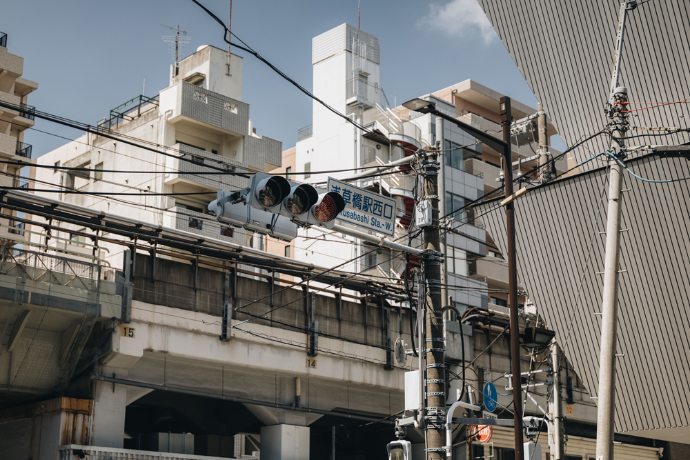 Traffic lights, signs and buildings layered across a busy Tokyo street in midday sunlight