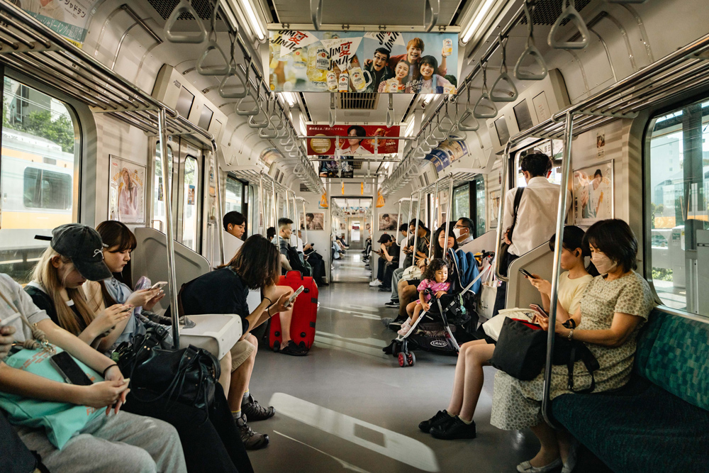 Passengers seated and standing inside a Tokyo train with bright daylight through the windows