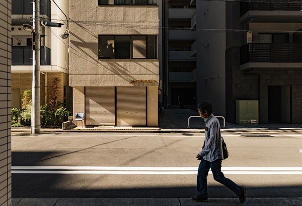 Person walking through a sunlit Tokyo street framed by deep architectural shadows