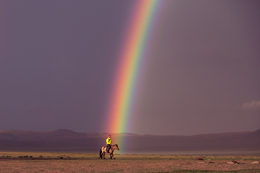 Landscape image of man on horse at rainbow