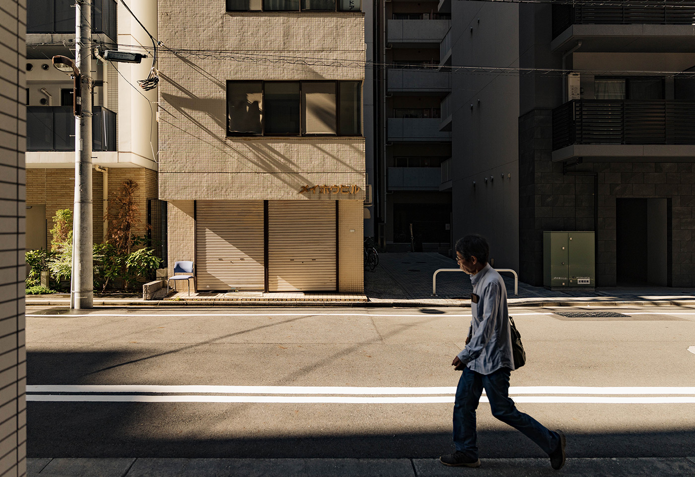 Person walking through a sunlit Tokyo street framed by deep architectural shadows